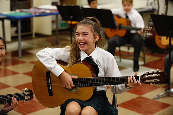 Girl smiling and playing guitar in Grade 6 music class